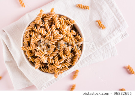 Raw pasta from buckwheat flour in a bowl and groats in a bowl on a pink. Top view. Closeup Raw pasta from buckwheat flour in a bowl and groats in a bowl on a pink. Top view. Closeup 96882695