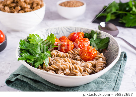 A bowl with buckwheat pasta, tomatoes and parsley leaves on the table. Vegetarian food A bowl with buckwheat pasta, tomatoes and parsley leaves on the table. Vegetarian food 96882697
