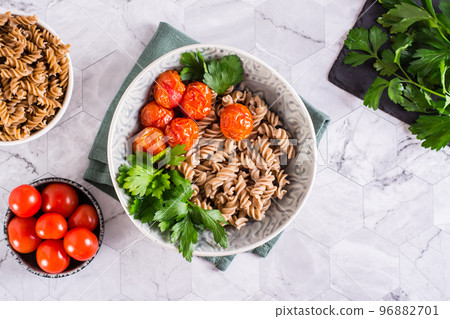 A bowl with buckwheat pasta, tomatoes and parsley leaves on the table. Vegetarian food. Top view A bowl with buckwheat pasta, tomatoes and parsley leaves on the table. Vegetarian food. Top view 96882701
