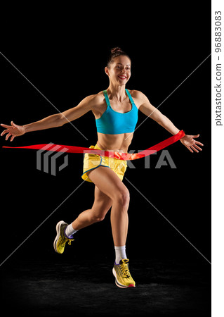 Winner, champion at finish line. Young fitness sportive girl in sports uniform running, training isolated over dark background. Sport, success, motivation 96883083