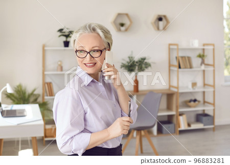 Friendly senior business woman having business conversation on mobile phone in her office. Friendly senior business woman having business conversation on mobile phone in her office. 96883281