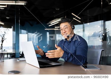Asian with a headset is talking on video call, man inside office smiling and gesturing joyfully in an online meeting, a businessman is telling his colleagues, a customer service tech support worker. Asian with a headset is talking on video call, man inside office smiling and gesturing joyfully in an online meeting, a businessman is telling his colleagues, a customer service tech support worker. 96883490