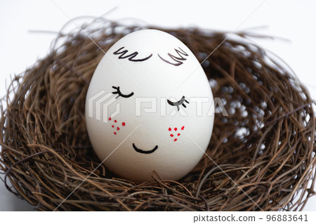 Close up of a beautiful white egg in a wicker nest on a white background. Cute face with red freckles. The view is straight. Spring postcard. Happy Easter. Close up of a beautiful white egg in a wicker nest on a white background. Cute face with red freckles. The view is straight. Spring postcard. Happy Easter. 96883641