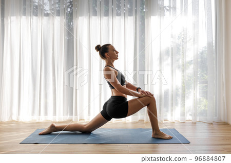 Young woman doing low lunge yoga pose during moring yoga training Young woman doing low lunge yoga pose during moring yoga training 96884807