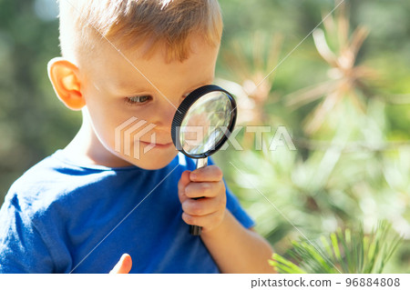 Curious boy is exploring nature with magnifying glass outdoors 96884808