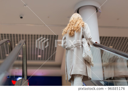 Young woman with long blond hair moving up on escalator 96885176
