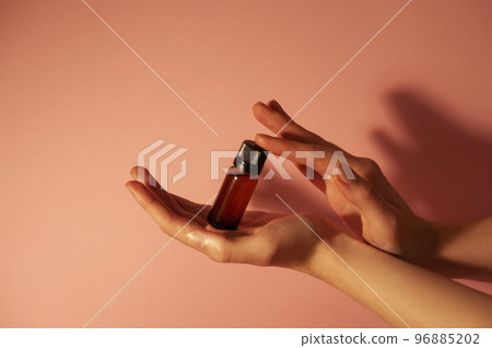 Brown bottle in beautiful hands on a peachy light background. Brown bottle in beautiful hands on a peachy light background. 96885202
