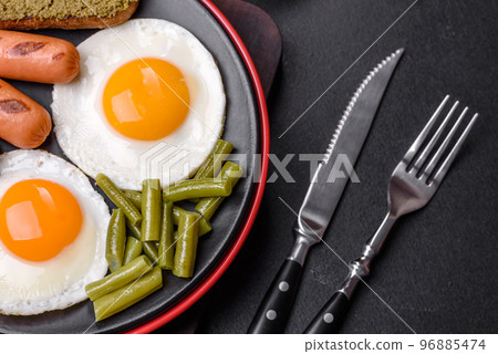 Tasty English breakfast of fried eggs, beans, asparagus, sausages with spices and herbs 96885474