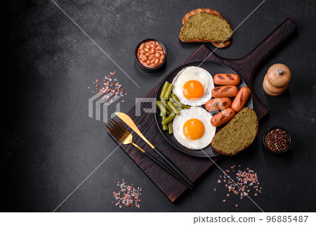 Tasty English breakfast of fried eggs, beans, asparagus, sausages with spices and herbs Tasty English breakfast of fried eggs, beans, asparagus, sausages with spices and herbs 96885487