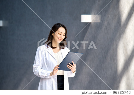 A smiling female doctor in a lab coat checking a medical record at the hospital 96885743