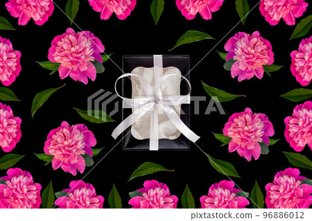 Black gift box with silver ribbon with peony flowers green leaves on dark background flat lay. Classic present package. 96886012