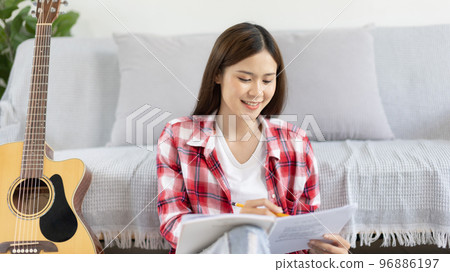 Asian woman specializes in music is composing the lyrics and melody for the opening of a new single, Using imagination and concentration in creating music, acoustic guitar, Creation of music notes. 96886197