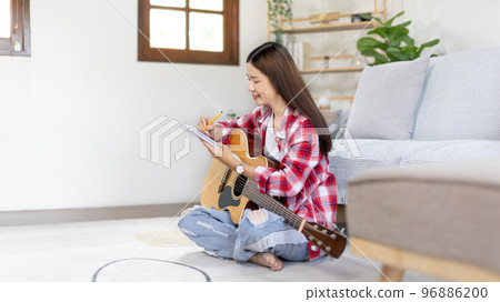 Asian woman specializes in music is composing the lyrics and melody for the opening of a new single, Using imagination and concentration in creating music, acoustic guitar, Creation of music notes. 96886200