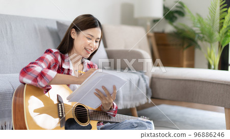 Asian woman specializes in music is composing the lyrics and melody for the opening of a new single, Using imagination and concentration in creating music, acoustic guitar, Creation of music notes. 96886246