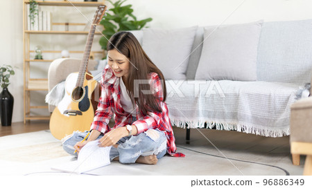 Asian woman specializes in music is composing the lyrics and melody for the opening of a new single, Using imagination and concentration in creating music, acoustic guitar, Creation of music notes. 96886349
