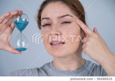 Caucasian red-haired woman holds an hourglass and examines the wrinkles around her eyes. Aging concept. 96886620