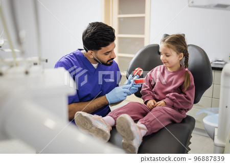 Young confident bearded pediatric dentist showing to little preschool girl how to brush teeth 96887839