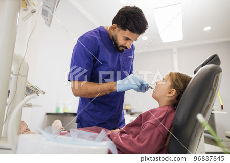 Confident bearded dentist examines the oral cavity of a young beautiful girl 96887845