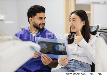 Male confident dentist showing x ray picture to attractive young patient 96887879