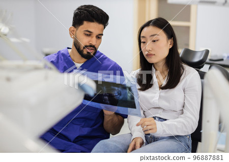 Male confident dentist showing x ray picture to attractive young patient 96887881