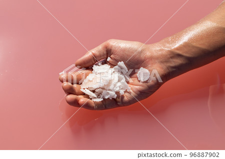 Hand holding salt crystals near pink water surface 96887902