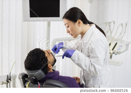 Asian dentist treating teeth of a young bearded man using tooth drill 96888526