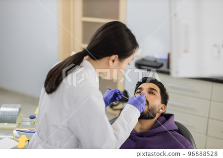 Asian dentist examines the oral cavity of young bearded handsome man Asian dentist examines the oral cavity of young bearded handsome man 96888528