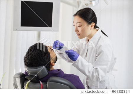 Asian dentist examines the oral cavity of young bearded handsome man 96888534