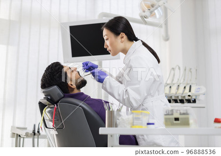 Asian dentist examines the oral cavity of young bearded handsome man 96888536