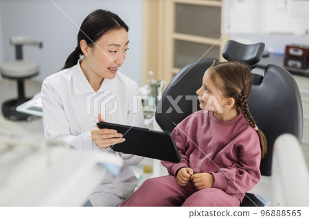 Female smiling asian dentist showing tablet pc computer to happy kid patient, 96888565
