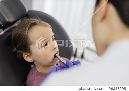 Girl lying on dentist chair with open mouth, female doctor curing her teeth, using dental drill. 96888598