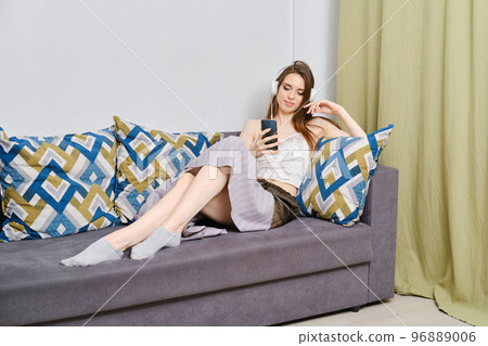 Young and calm woman lying on couch in headphones listening to music or radio station 96889006