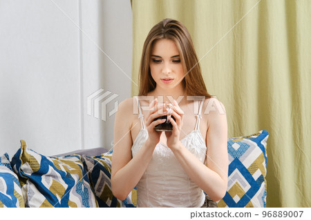 Cute young woman holds cup of coffee with both arms Cute young woman holds cup of coffee with both arms 96889007
