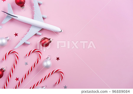 Christmas travel concept. Model of passenger plane and candy canes on pink background Christmas travel concept. Model of passenger plane and candy canes on pink background 96889084