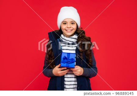 happy child in puffer jacket and hat hold box. kid with present. teen girl on red background 96889145