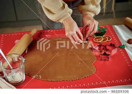 Woman preparing gingerbread cookies at kitchen. Female hands cutting ginger dough with cutter to making cookies for winter holidays Woman preparing gingerbread cookies at kitchen. Female hands cutting ginger dough with cutter to making cookies for winter holidays 96889306