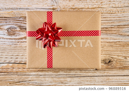 Above view of festive gift box wrapping in craft paper with festive ribbons and bow. Present for Christmas holidays on wooden background Above view of festive gift box wrapping in craft paper with festive ribbons and bow. Present for Christmas holidays on wooden background 96889316