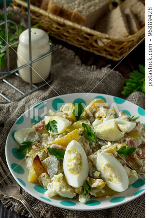 Salad with baked potatoes, pickled cucumber, egg and smoked turkey on a festive table in a rustic style. Salad with baked potatoes, pickled cucumber, egg and smoked turkey on a festive table in a rustic style. 96889428