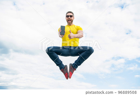 man jumping and presenting smartphone on sky background. thumb up 96889508