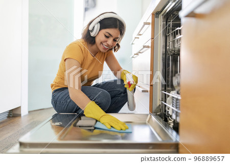 Happy Arab Female Cleaning Washing Machine In Kitchen With Rag And Sprayer Happy Arab Female Cleaning Washing Machine In Kitchen With Rag And Sprayer 96889657