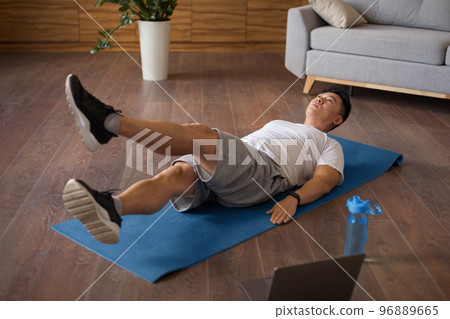 Mature korean man doing exercises for legs and abs on mat in living room interior and watching workout on laptop Mature korean man doing exercises for legs and abs on mat in living room interior and watching workout on laptop 96889665