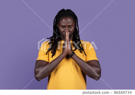 African american young man praying with closed eyes on purple African american young man praying with closed eyes on purple 96889734