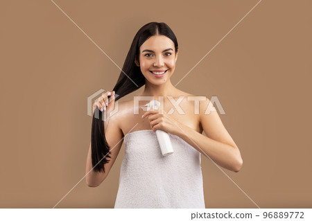 Smiling long-haired adult woman using hair spray, copy space 96889772