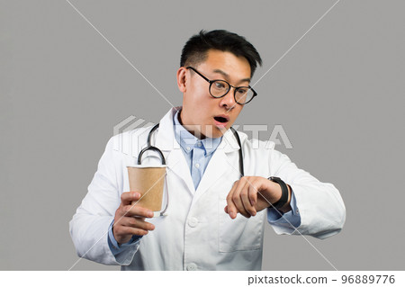 Shocked funny mature chinese male therapist in white coat, glasses with cup of coffee takeaway looks at watch 96889776