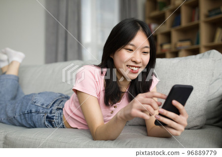 Asian lady enjoy spare time alone, lying on sofa and watching news on cellphone, relaxing at home Asian lady enjoy spare time alone, lying on sofa and watching news on cellphone, relaxing at home 96889779