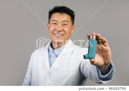 Smiling mature chinese male therapist in white coat showing inhaler for breathing and asthmatic attack Smiling mature chinese male therapist in white coat showing inhaler for breathing and asthmatic attack 96889799