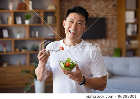 Happy asian mature man holding fork and bowl with fresh vegetable salad, eating healthy lunch after domestic training Happy asian mature man holding fork and bowl with fresh vegetable salad, eating healthy lunch after domestic training 96889801