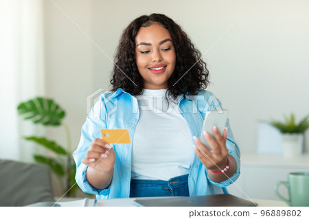 Mobile shopping. Happy black body positive lady using smartphone and shopping online with credit card Mobile shopping. Happy black body positive lady using smartphone and shopping online with credit card 96889802