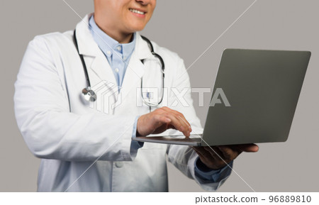 Happy mature chinese male therapist in white coat with stethoscope typing on computer, cropped, close up 96889810