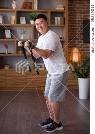 Excited active korean middle aged man working out with resistance band in living room interior and smiling at camera 96889811
